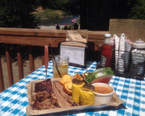 plate of smoked meat, corn on the cob and watermelon with beverage on table on restaurant patio
