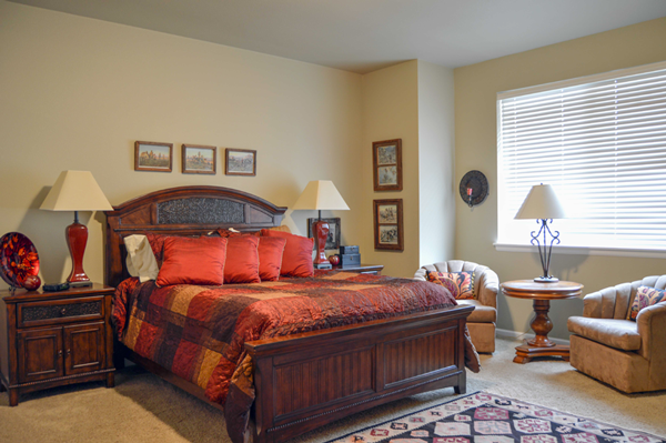 Guest room at vacation rental with bed, two nightstands with lamps and sitting area next to a window