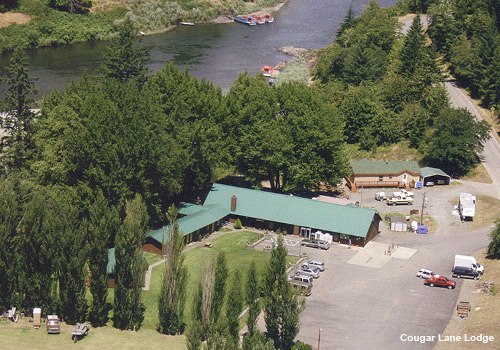 aerial view of lodge with parking lot, evergreen trees and river