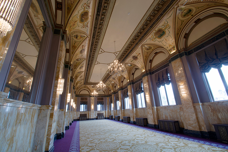 hallway of hotel with chandeliers and opulent molding and curtains on windows