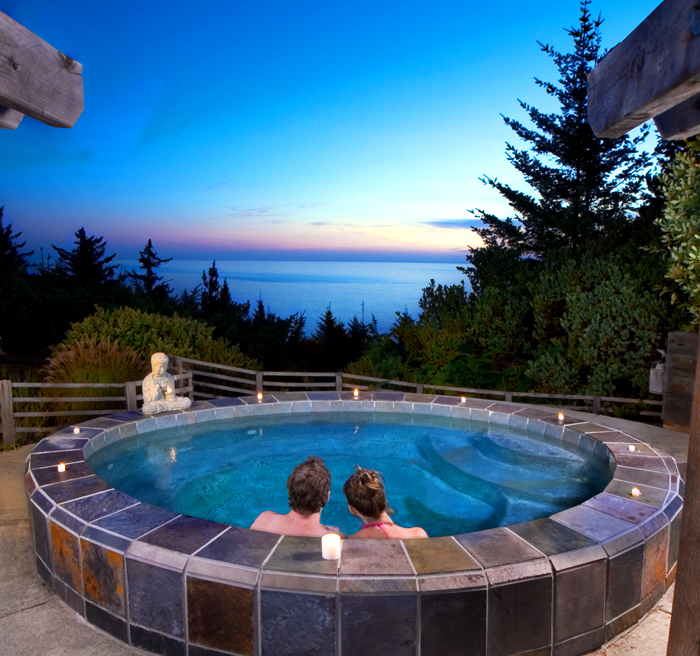 two people soaking in round hot tub looking out to a forest and ocean view