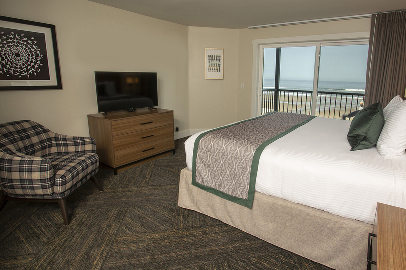 guest room of hotel with double bed, chair, entertainment center and view of beach out the window
