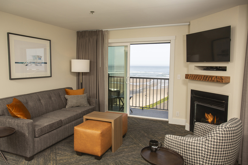 sitting room of hotel guest room with modern furniture, fireplace and view of the beach out the window