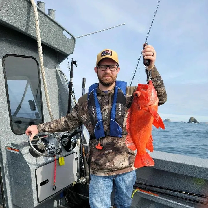 Fisherman holding bright orange fish on boat with ocean in background