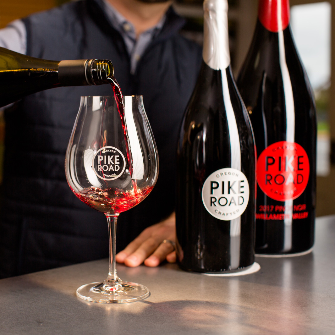 wine poured into pinot glass with wine bottles in background