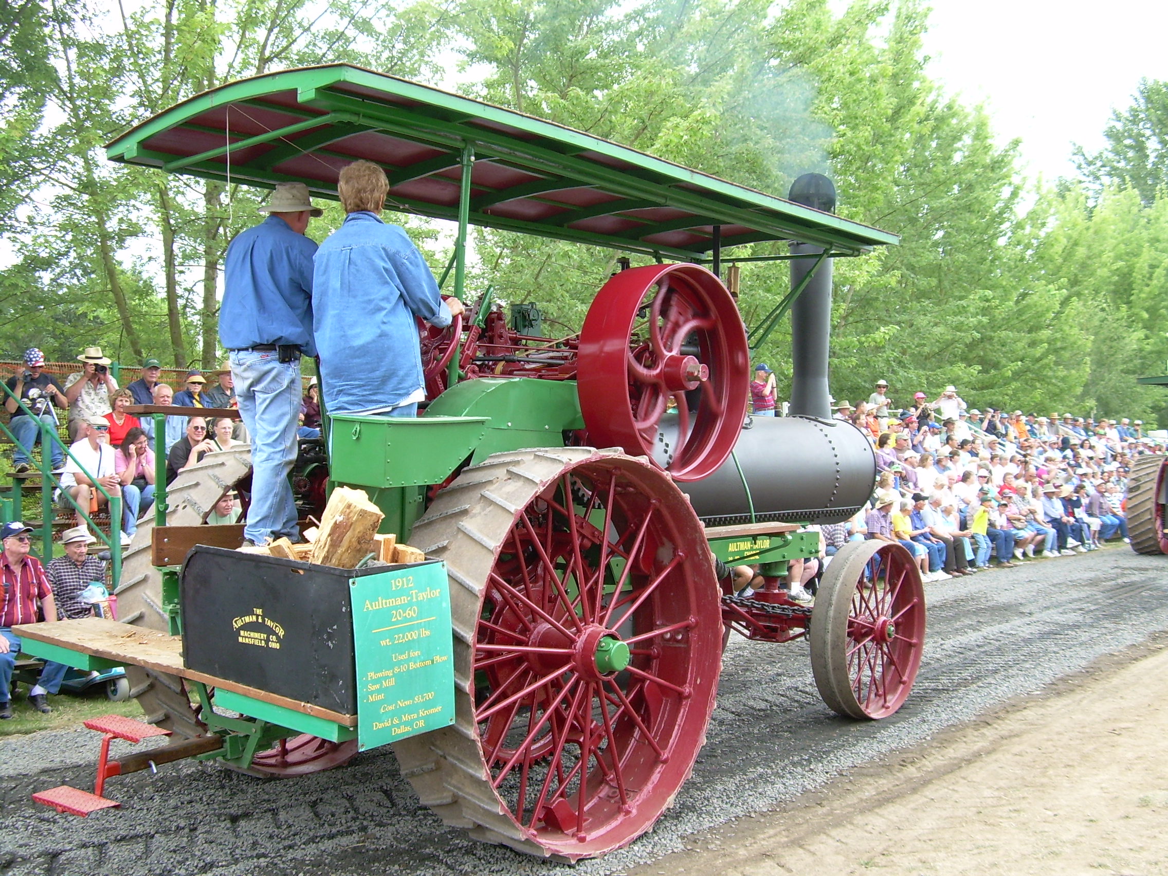 two people riding old steam engine as crowd looks on