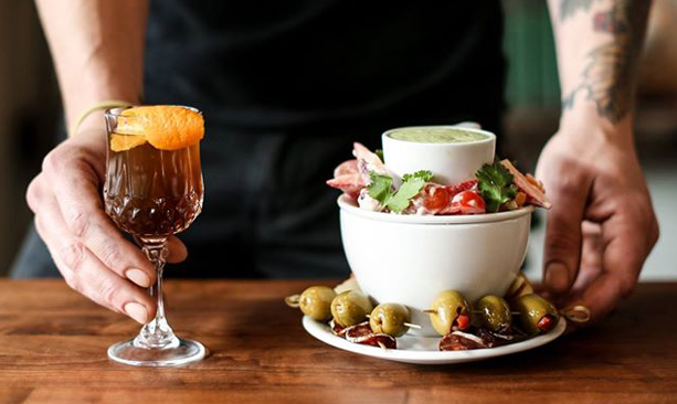 cocktail in vintage glass next to a plate and bowl of sliced meat and olives