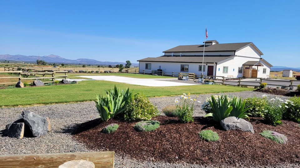 picture of a white barn building with a cement slab in grees grass with a wooden fence