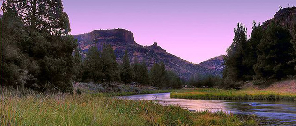 River flowing through a valley with mountains and trees at dusk.