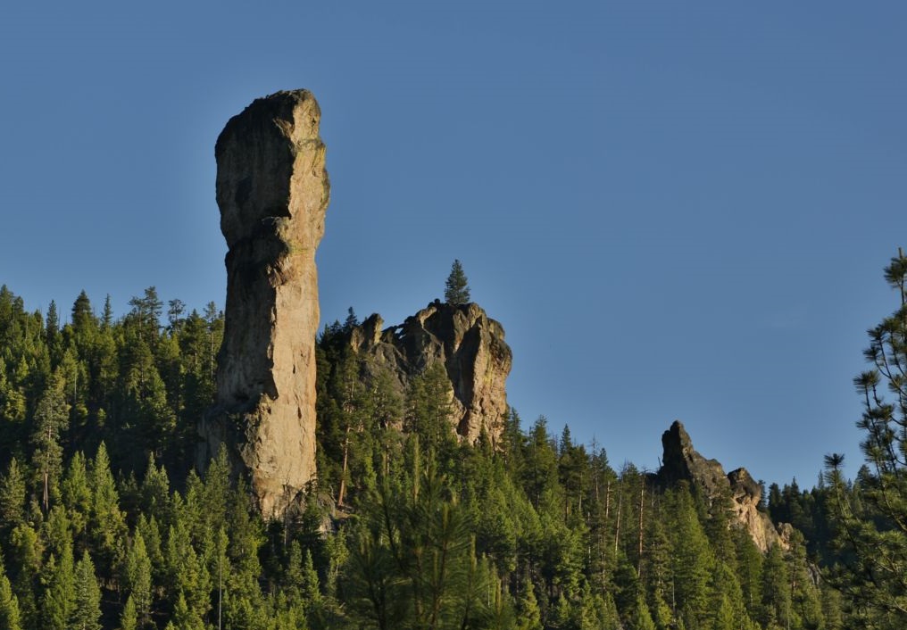 Rocky cliff with trees against a blue sky.