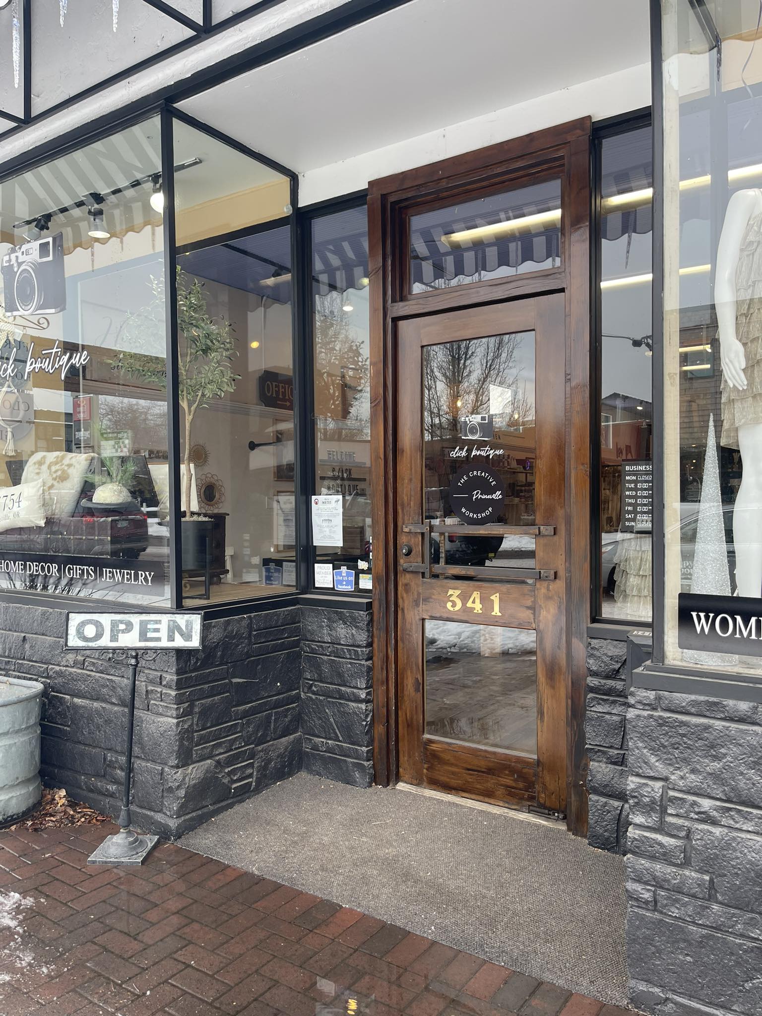 sidewalk with a wooden door with windows leading into a store surrounded by glass windows with black trim
