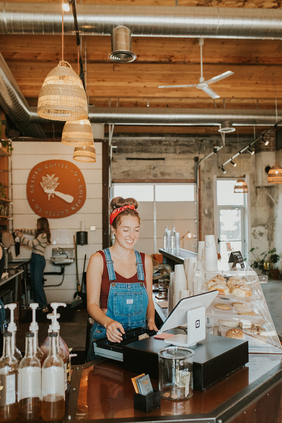 Woman in overalls and red bandana at square cash register at Golden Coffee in Prineville