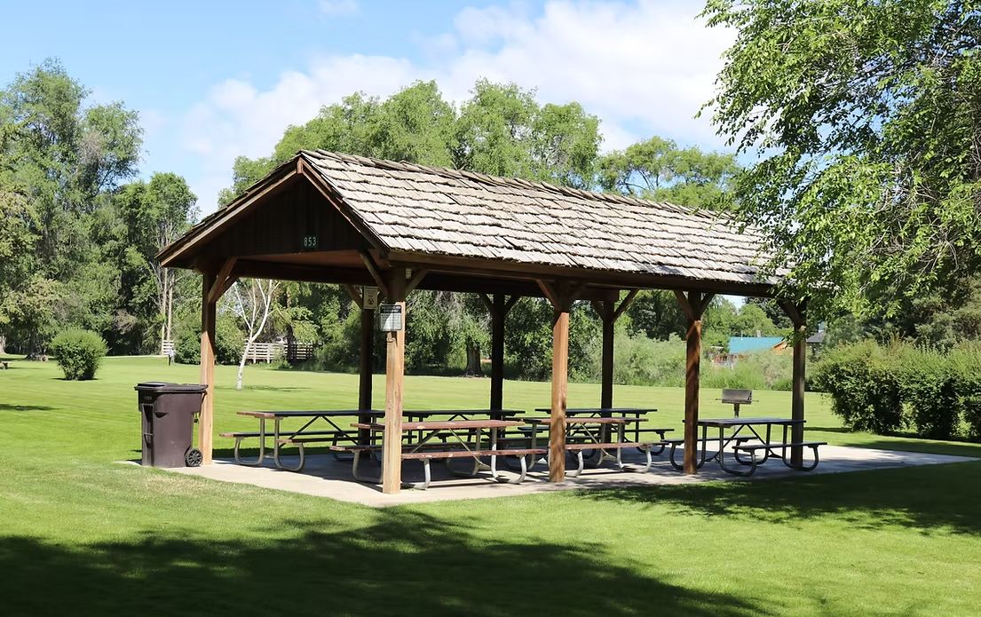 covered picnic area with picnic tables surrounded by green grass and tall elm tree