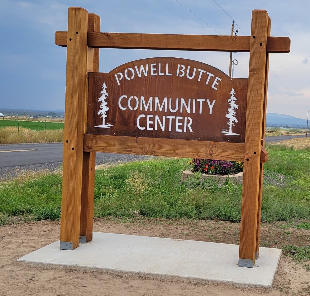 wooden sign with white carved trees on either side of the words Powell Butte Community Center