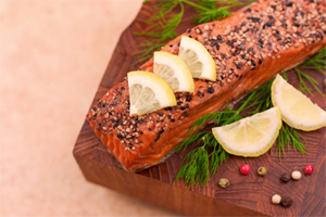 Grilled salmon with lemon slices and spices on a wooden board.