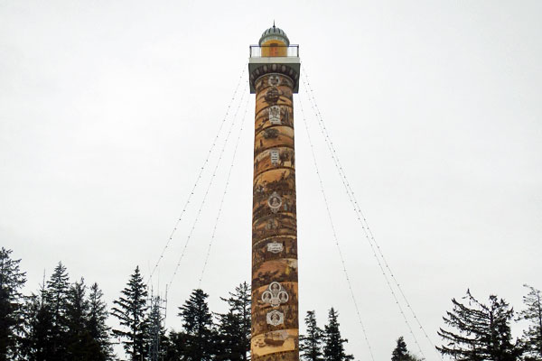 a column taller that the evergreen trees in the background