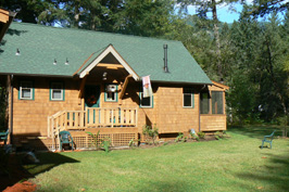 Cozy wooden cabin with green roof and porch in a wooded area.