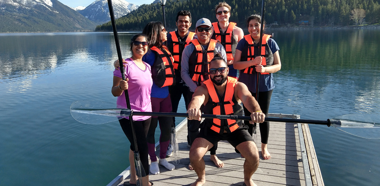 group of people holding paddles posing on a dock with lake and mountain in background