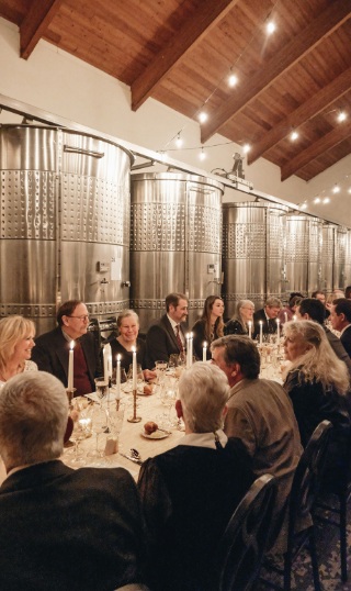 Seated diners at a long table in winery production room.