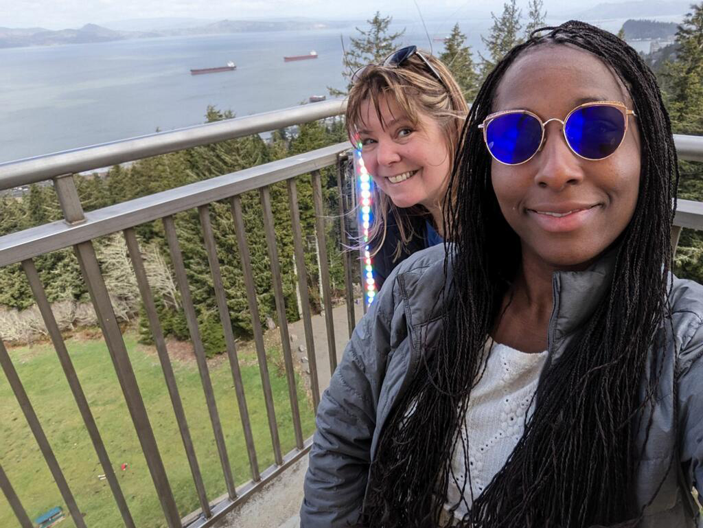 person wearing sunglasses takes selfie while another peeks from behind them