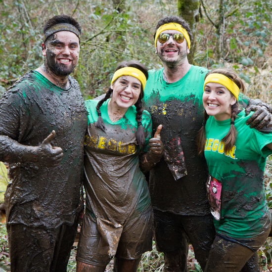 four people covered in mud smile at camera