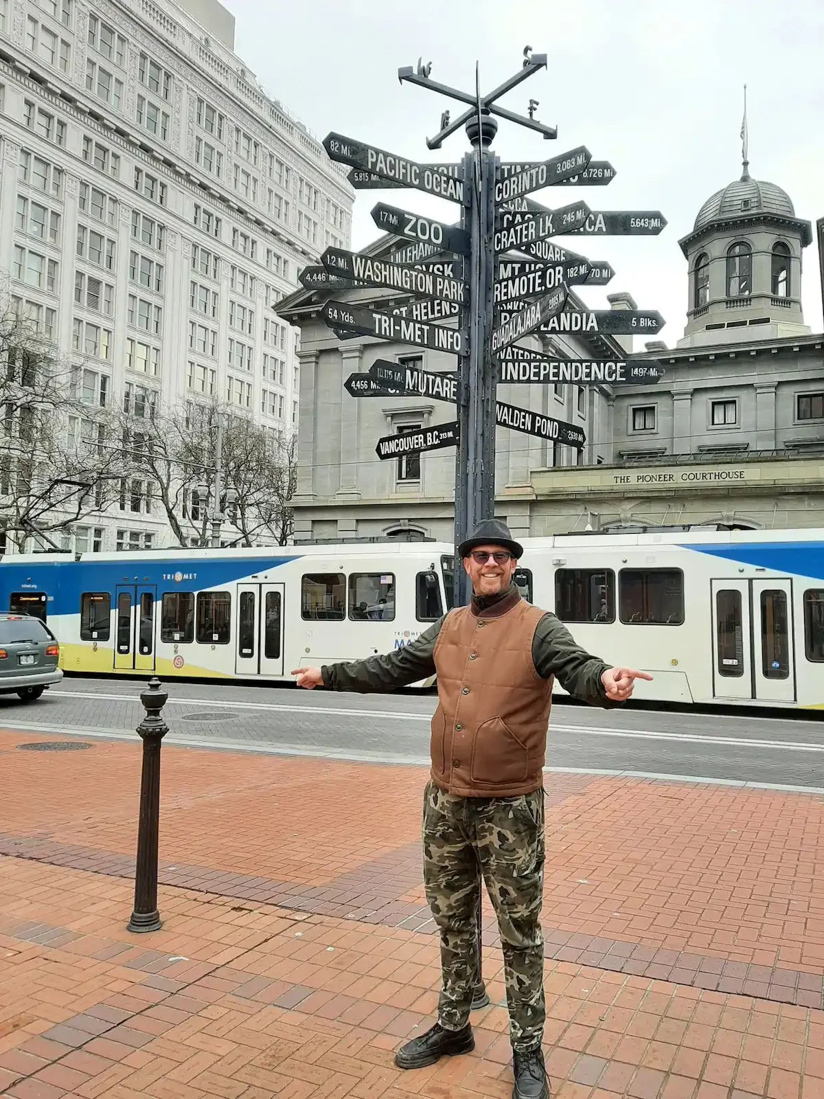 Man poses in front of directional sign and light rail train.