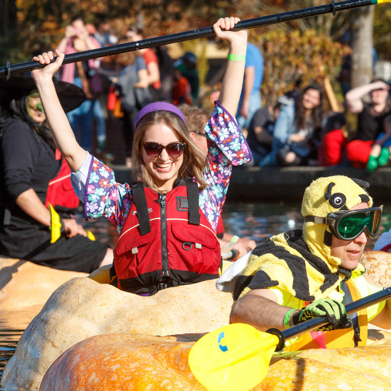 paddler in floating pumpkin holds paddle over head
