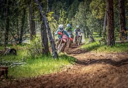 three people riding dirt bikes on trail in OHV park