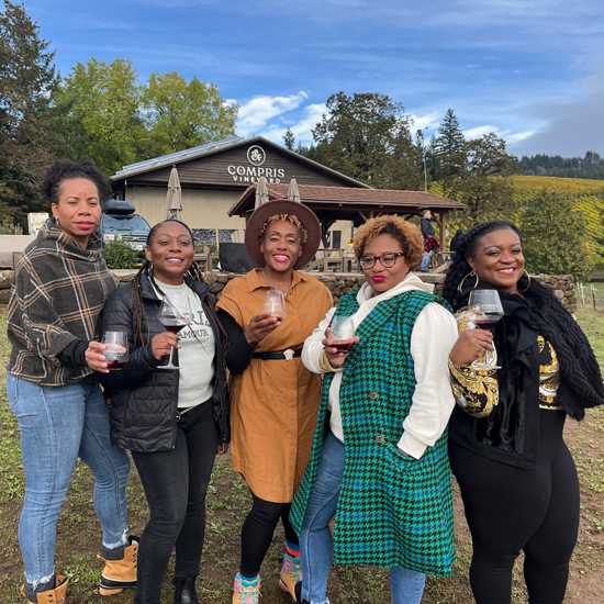 group of five people smiling and holding wine glasses in front of Compris Vineyards tasting room
