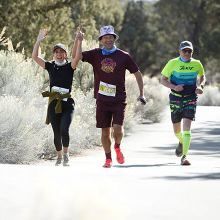 three runners on paved path two smiling holding hands with hands raised