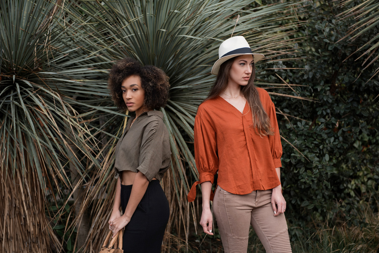 Two women standing next to each other in front of plants.
