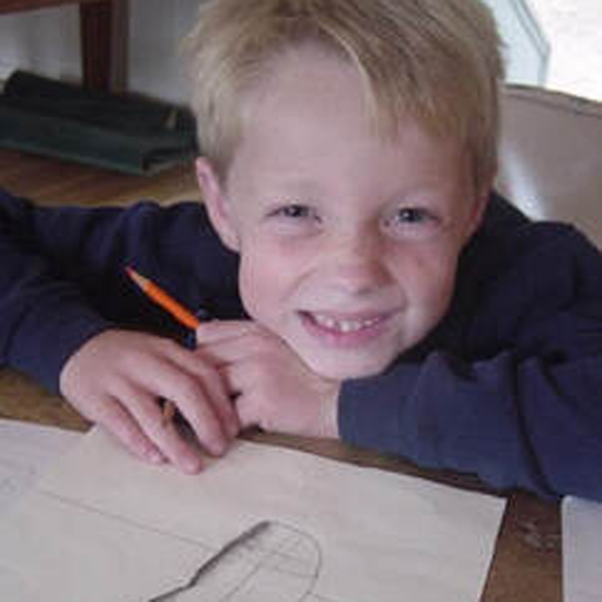 child smiles holding colored pencil and resting their head on their arm