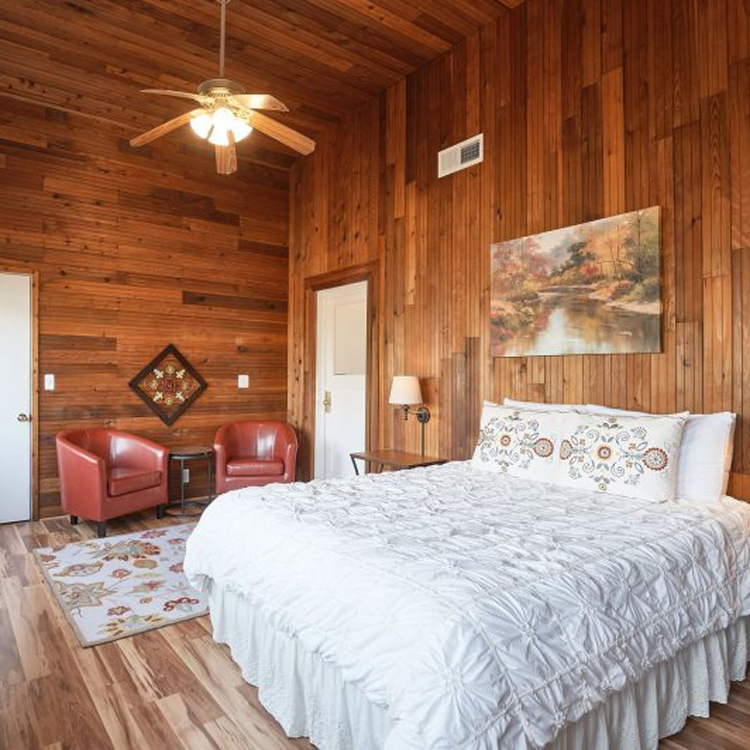 bedroom with wood panelling, high ceilings with ceiling fan and sitting chairs