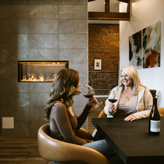 two people seated sip wine by a fireplace