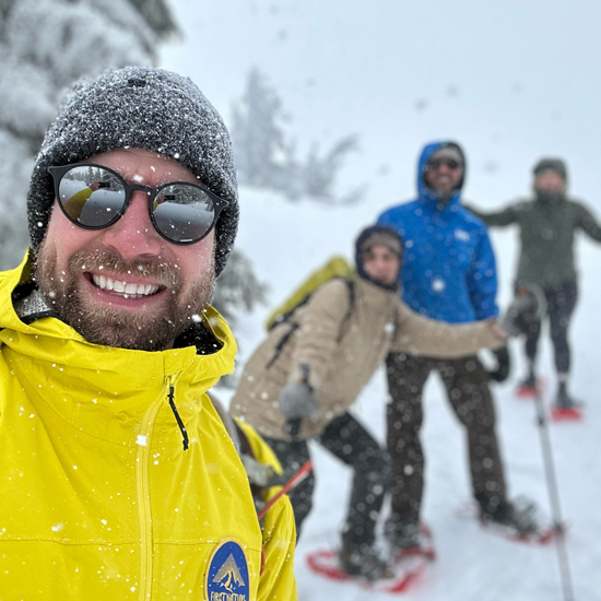 guide leading small group snowshoeing tour takes selfie with group