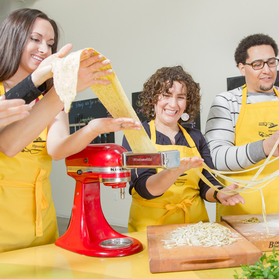 three people roll pasta in a KitchenAid pasta roller