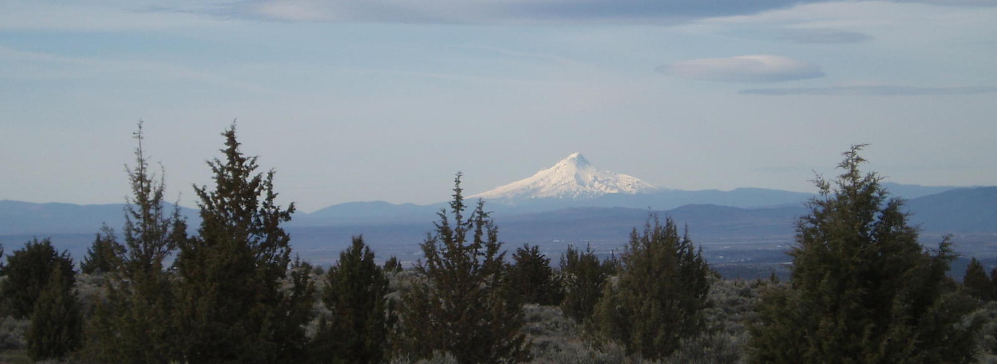 Snowy mountain peak with distant hills and trees.