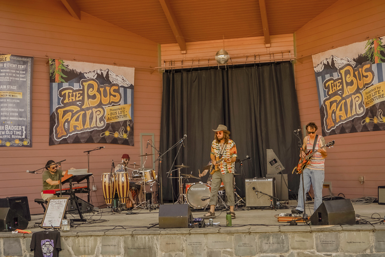a live band performing on an outdoor stage at The Bus Fair, a music and arts event.