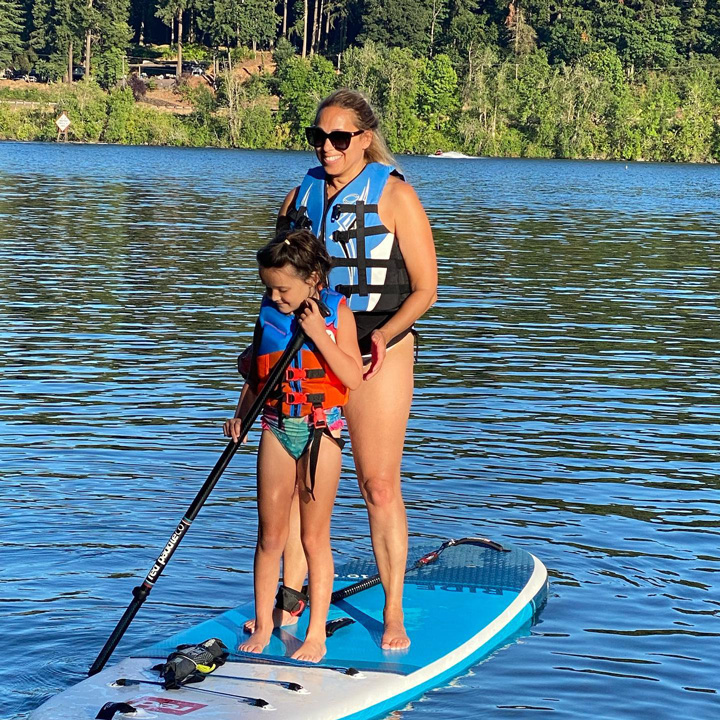 mother and daughter on stand up paddle board both wearing personal floatation devices