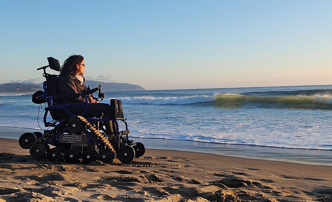 person operates all terrain wheelchair on a sandy beach