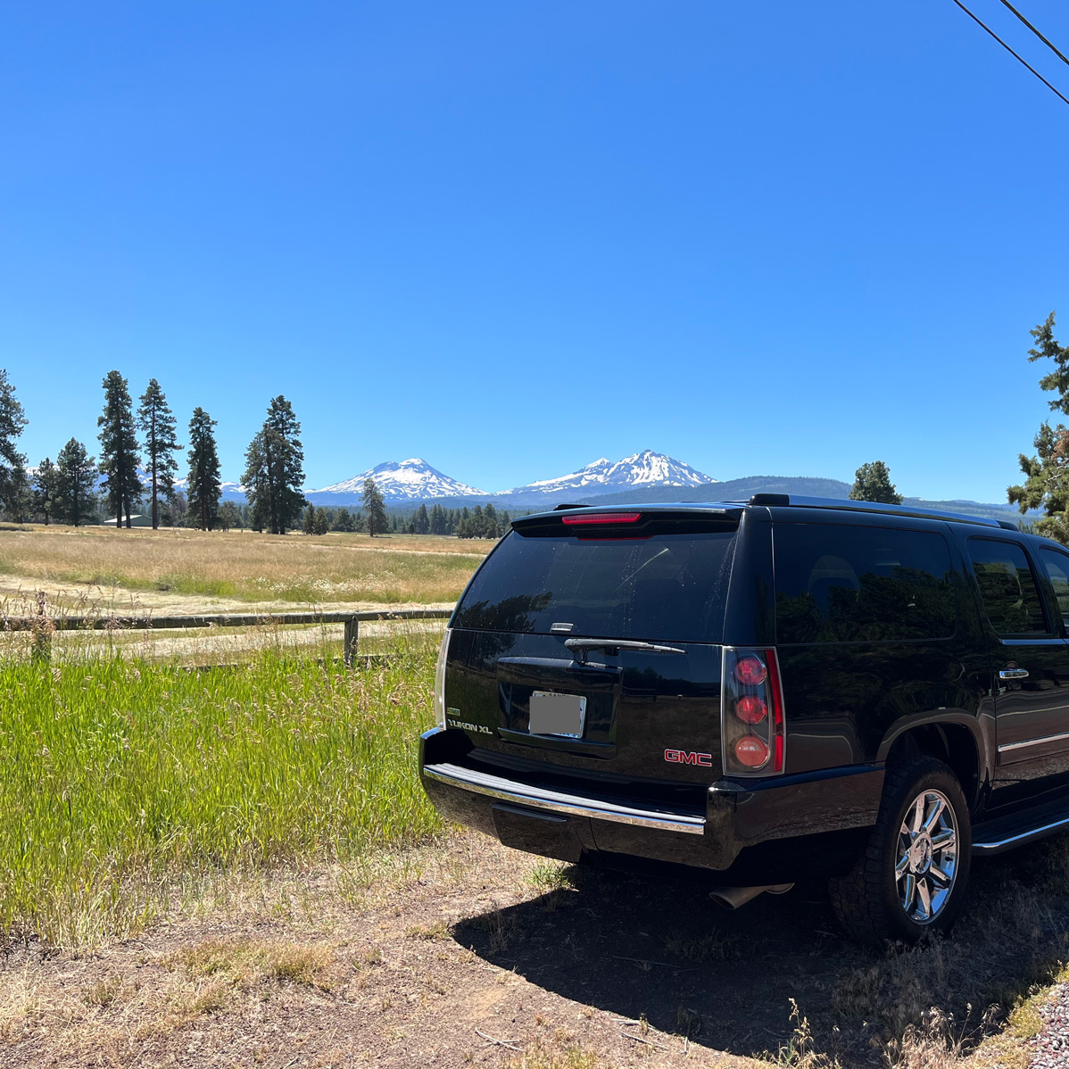 SUV parked on gravel road with mountains in the distance beneath a clear blue sky