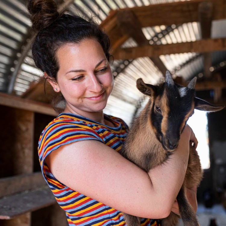 person smiling while holding baby goat