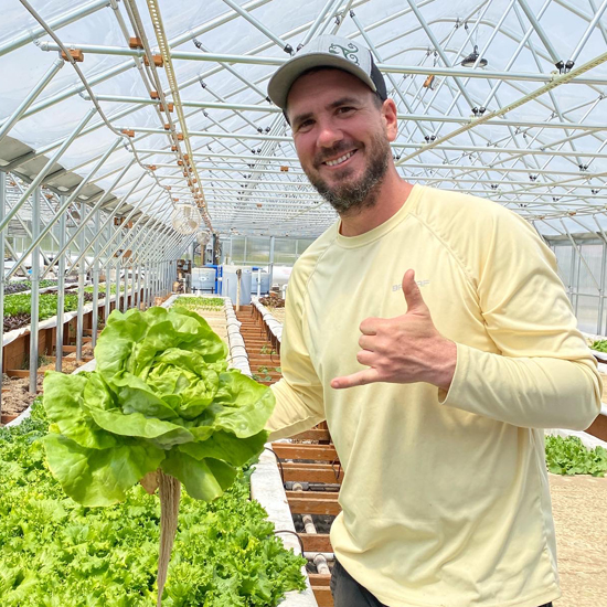 person holds large head of butter lettuce well signing hang loose with his free hand