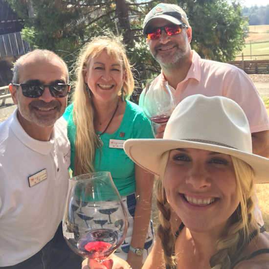 four people smiling while outside in a vineyard