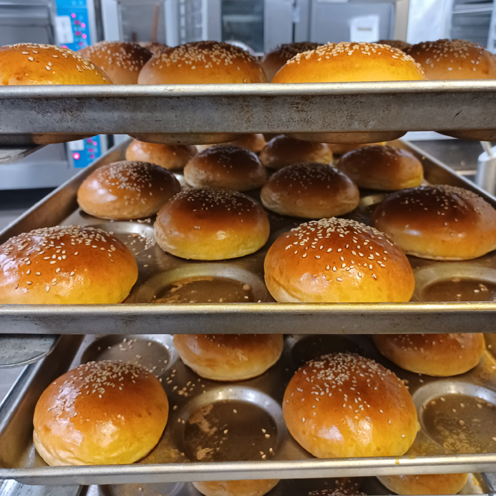 trays of bun shaped bread with sesame seed topping stacked in a tray cart