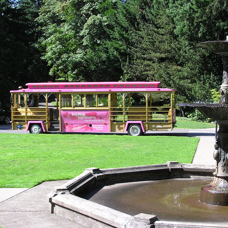 trolley parked near fountain with large trees in background