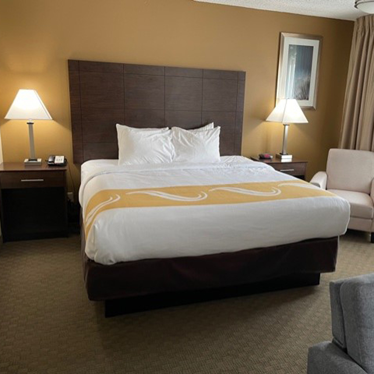 interior of hotel room with carpet, a double bed, two nightstands and lamps