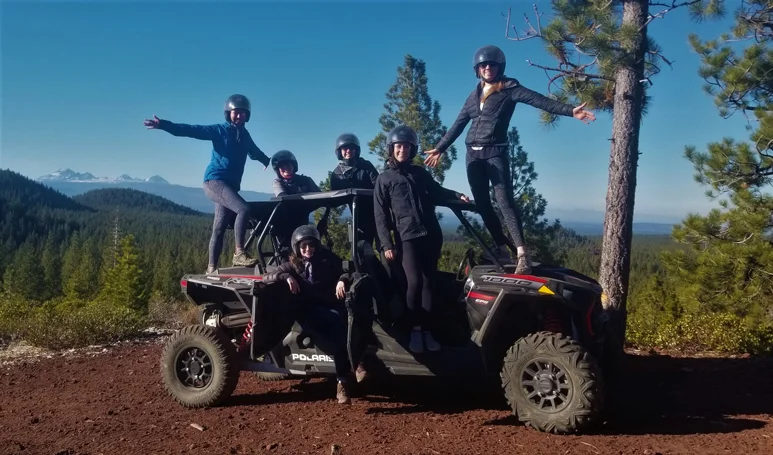 Six people wearing helmets pose with a dune buggy.