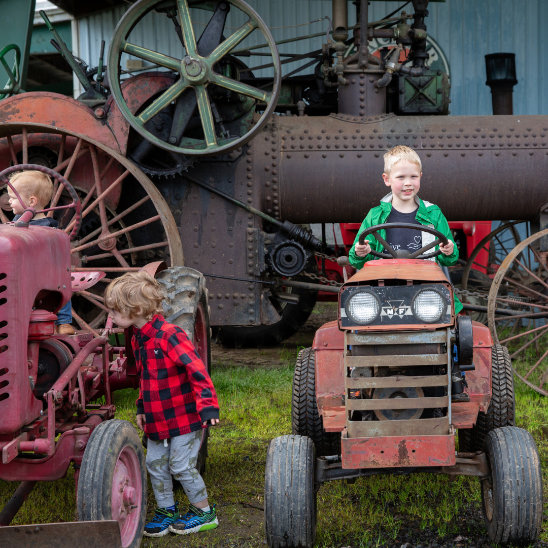 three children explore parked antique lawn trackers