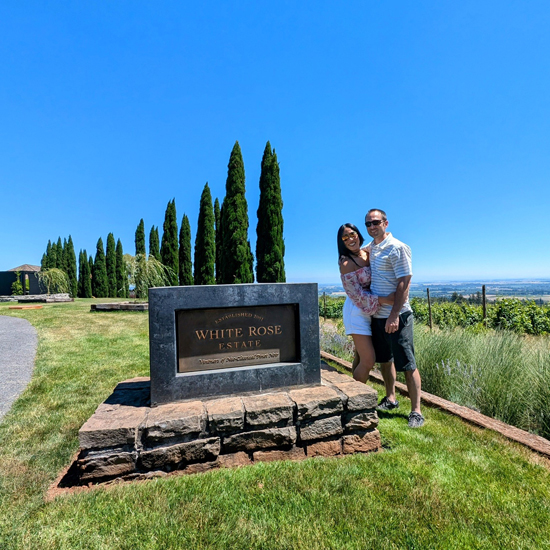 couple embraces while standing next to a sign for White Rose Estate winery